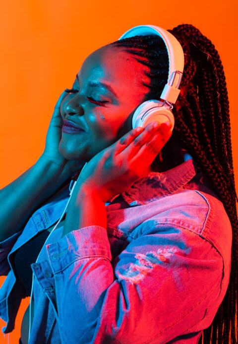 African american young woman listening to music online dancing and singing with headphones, neon