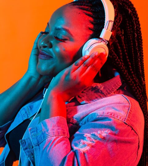 African american young woman listening to music online dancing and singing with headphones, neon