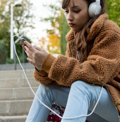 Portrait of a Young student girl sitting on the stairs. Listening some music.